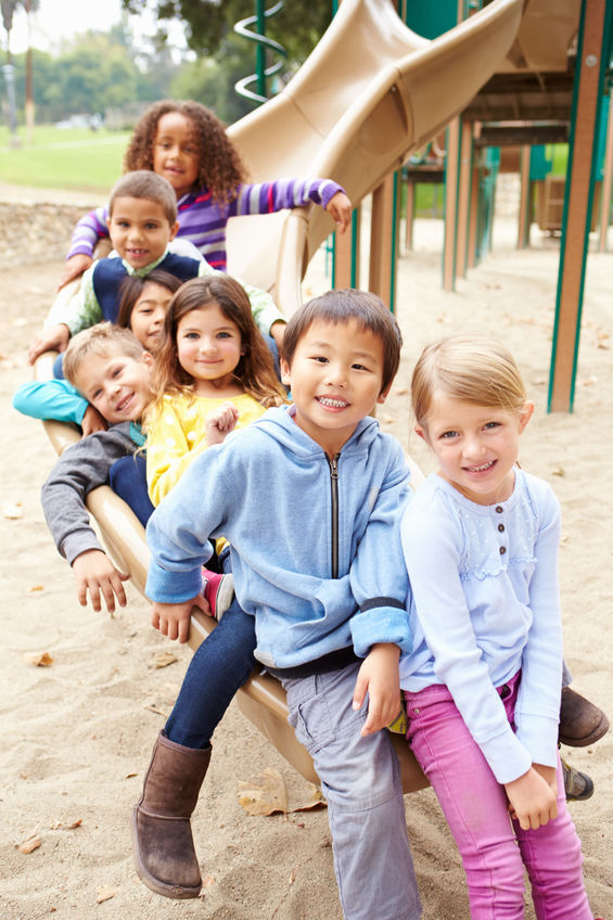 Group Of Young Children Sitting On Slide In Playground